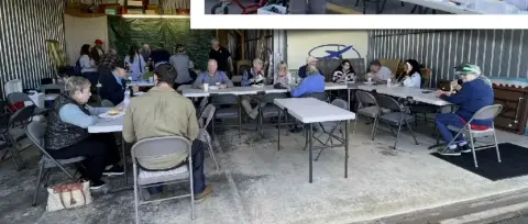 Members seated at long tables in a hangar during a gathering