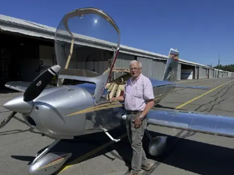 Pilot standing beside a silver low-wing airplane with the canopy open