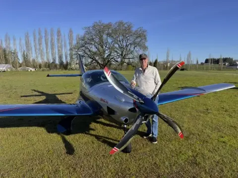 Pilot standing beside a blue low-wing amphibian on the grass