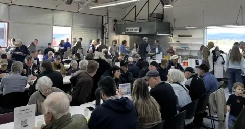 Crowd seated at breakfast tables inside a hangar