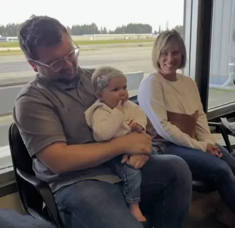 Man holding a toddler, seated next to a smiling woman