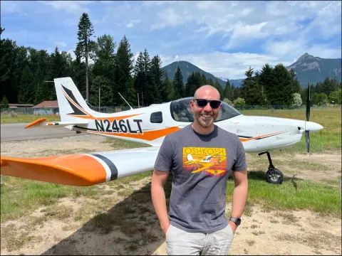 Man in sunglasses standing in front of a white and orange airplane