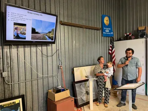 Presenters standing beside a screen in a hangar
