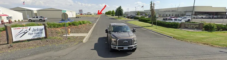 Street view of the airport entrance road. On the left is the Jackson Flight Center Learn to Fly sign; a red arrow points down the road to Rep. Dent's hangar, just past it.