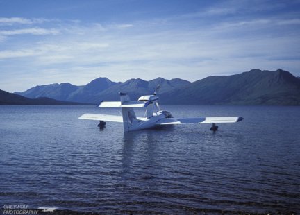 A white amphibian airplane on calm water with mountains behind