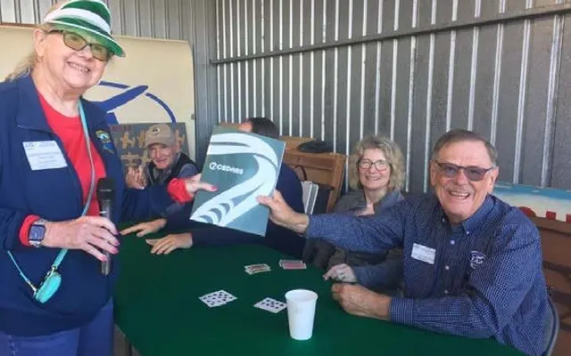 Chapter members laughing around a green card table in the hangar during the 2025 Poker Run