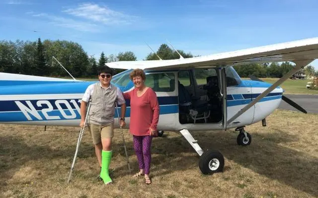 Emily and Aiden standing beside "Sally," a blue and white Cessna, on the grass