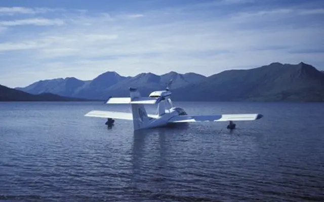 A white amphibian airplane on calm water with mountains behind