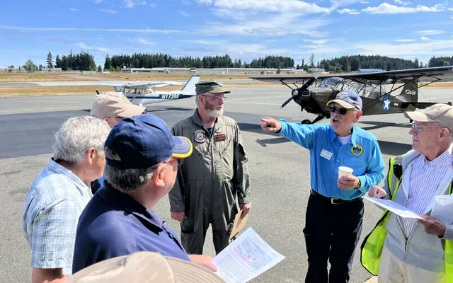 A volunteer in a blue shirt points across the ramp as he briefs pilots holding maps before the Young Eagles flights